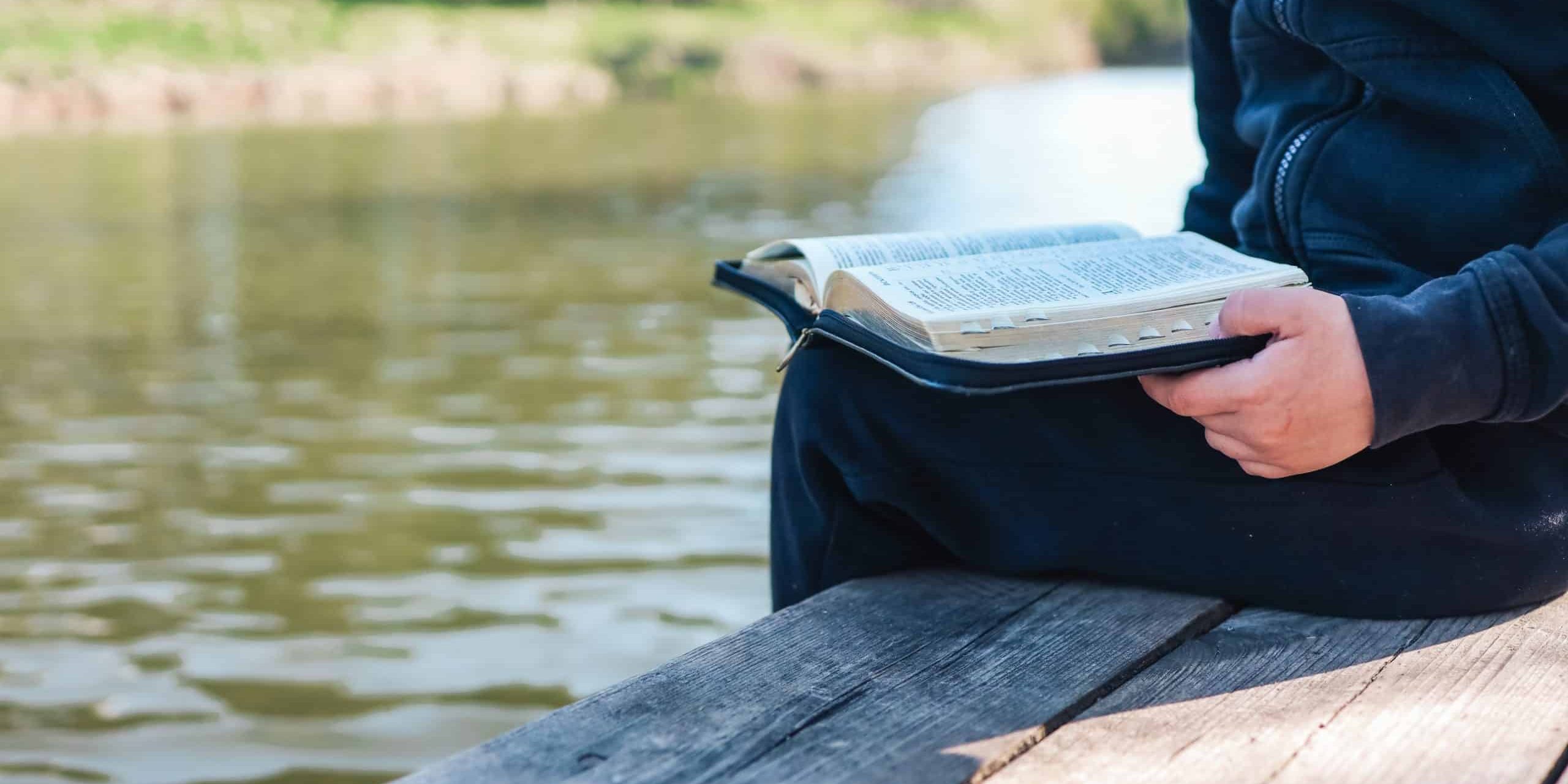 Child reads Bible book while sitting near pond. Christian illustration. Place for text.