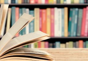 An open book is shown in front of a bookshelf full of books